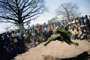 Un homme recouvert de la tête au x pieds de feuillages danse, entourés d'une large audience de spectateurs lors d'une cérémonie animiste pour les obsèques d'un homme, Bobo Dioulasso, Burkina Faso, 2007.