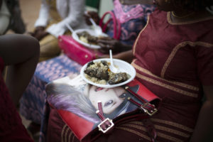 Gros plan en plongée d'una assiette en plastique contenant du riz et du poisson posé sur un sac à main faisant office de table sur les genoux d'une femme, Ouagadougou, Burkina Faso, 2016.
