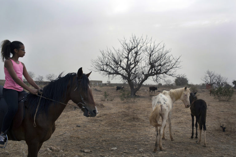 Une jeune fille sur son cheval au milieu d'un terrain vague à Ouagadougou, Burkina Faso, 2016.