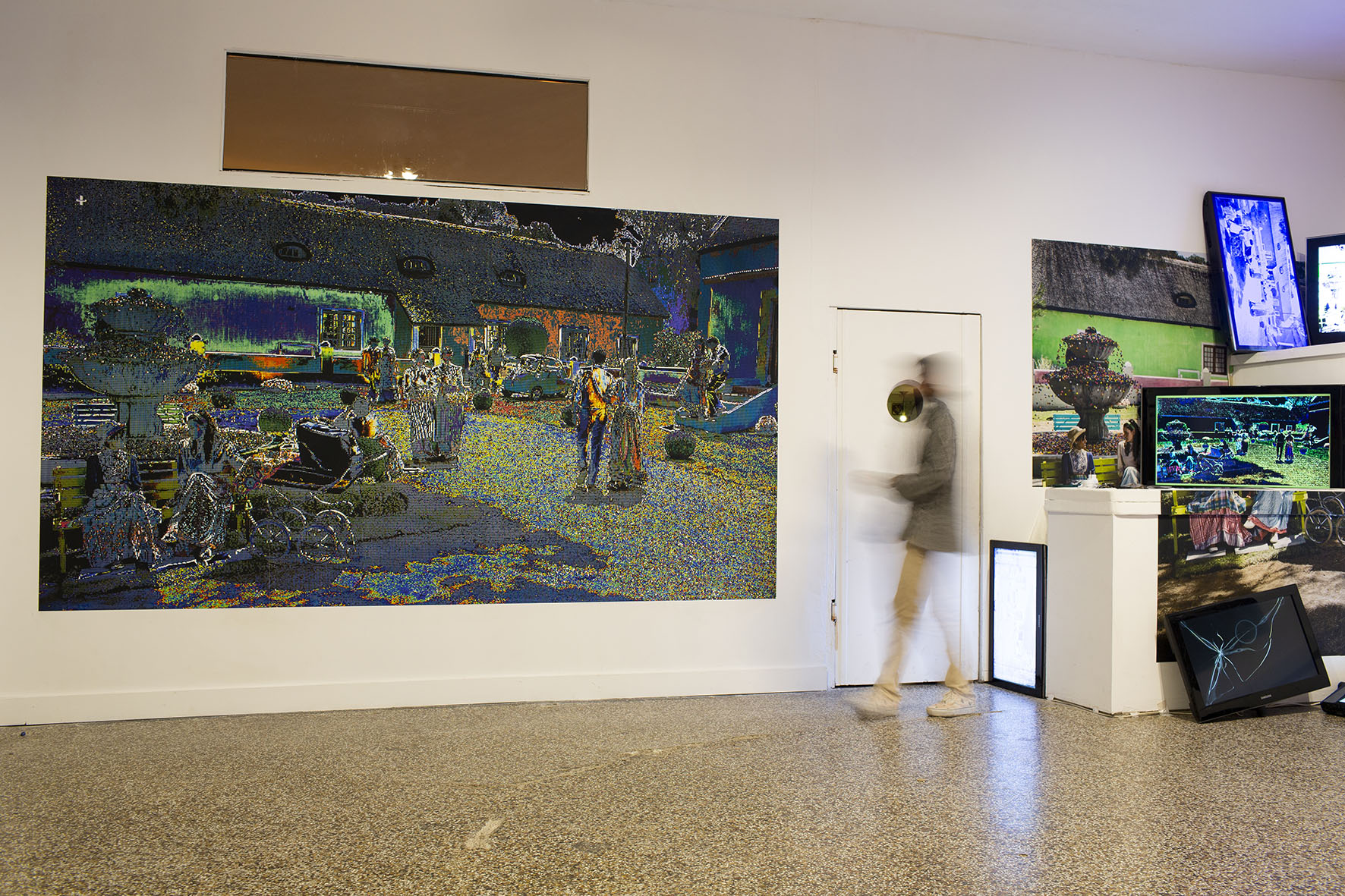 Vue d'exposition dans une galerie : un grand tirage papier peint de dimension 2x3 mètres est présenté à côté d'une installation en volume composée d'écrans défecteux.